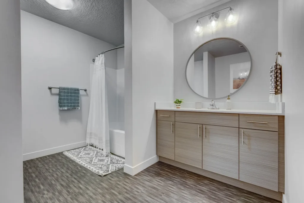 large bathroom with circle wall mirror and bathtub and cabinets